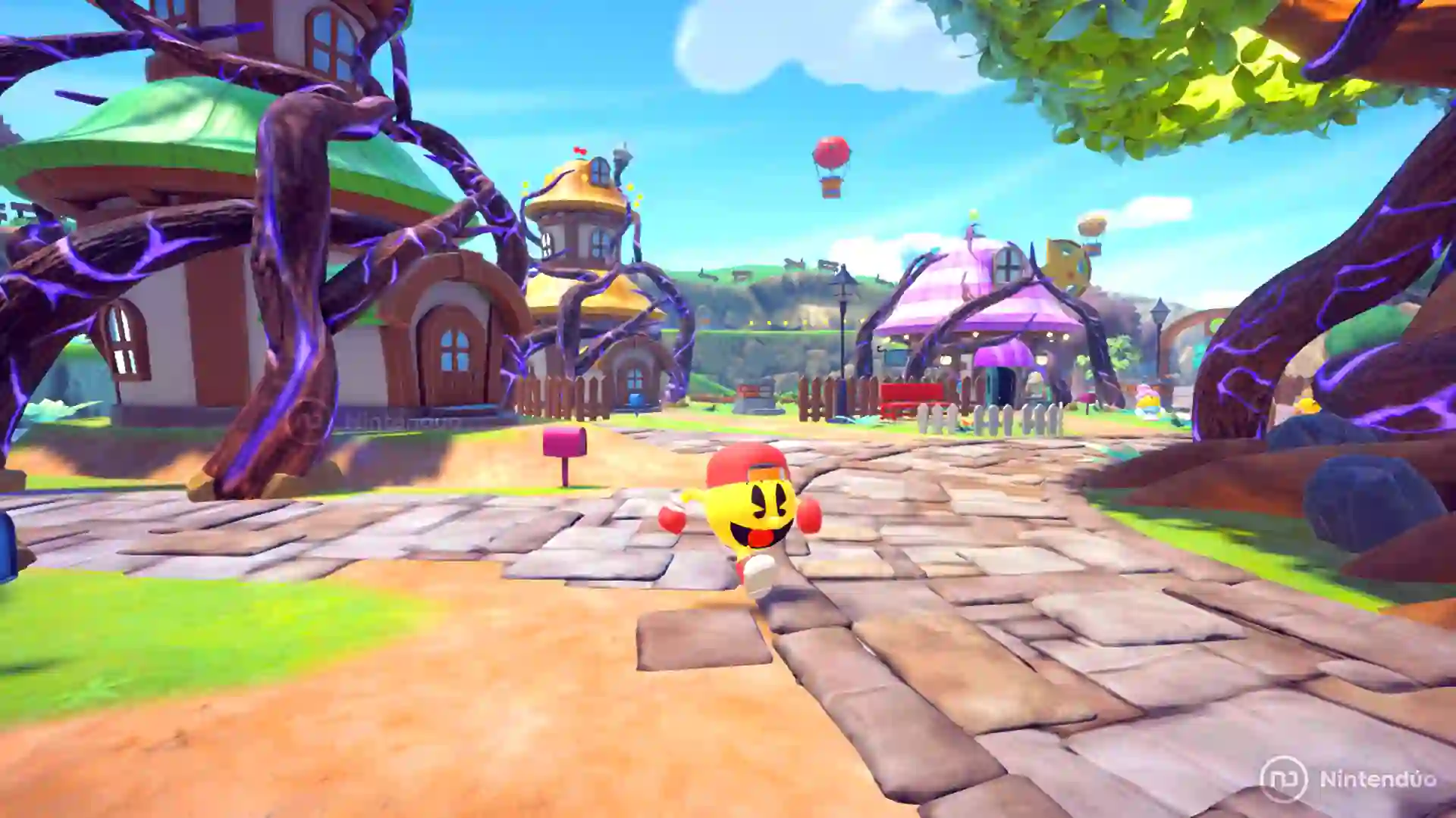 Captura de Pac‑Man World 2 Re‑Pac donde Pac‑Man corre por un pintoresco pueblo con casas redondas y árboles retorcidos bajo un cielo despejado.