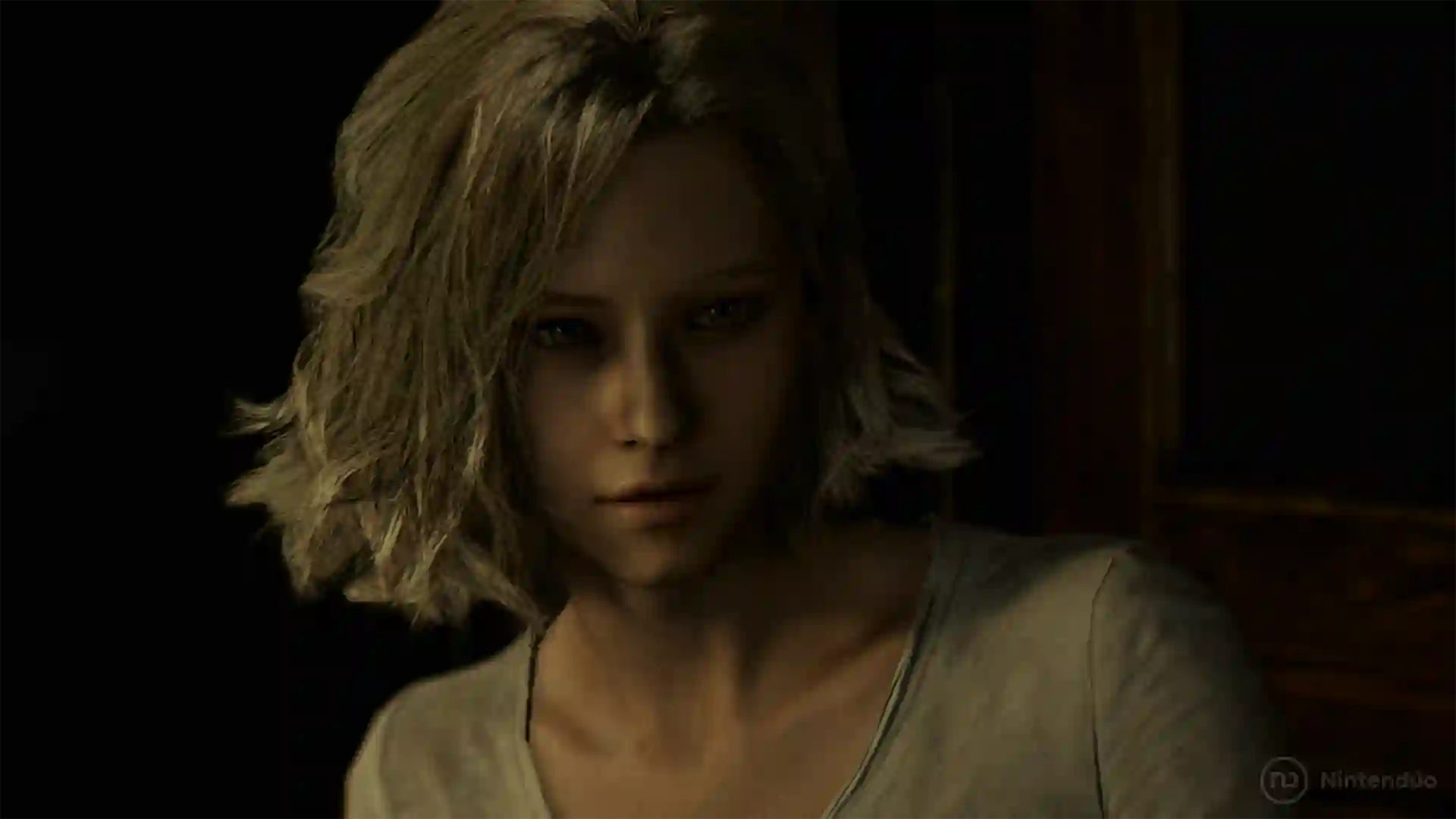 Resident Evil Requiem: primer plano de una mujer rubia de cabello corto con expresión seria en una habitación oscura.