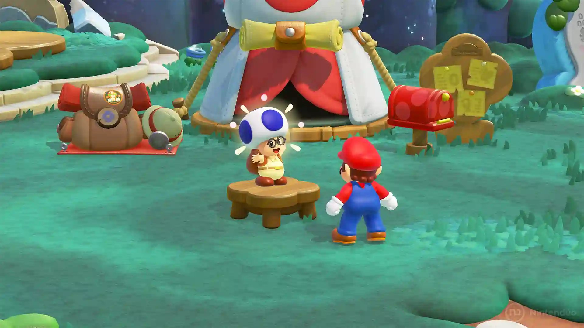 Super Mario Bros. Wonder – Nintendo Switch 2 Edition: Mario habla con Toad en un campamento verde con una tienda circular de colores blanco y rojo, una mesa de madera y diversos accesorios.