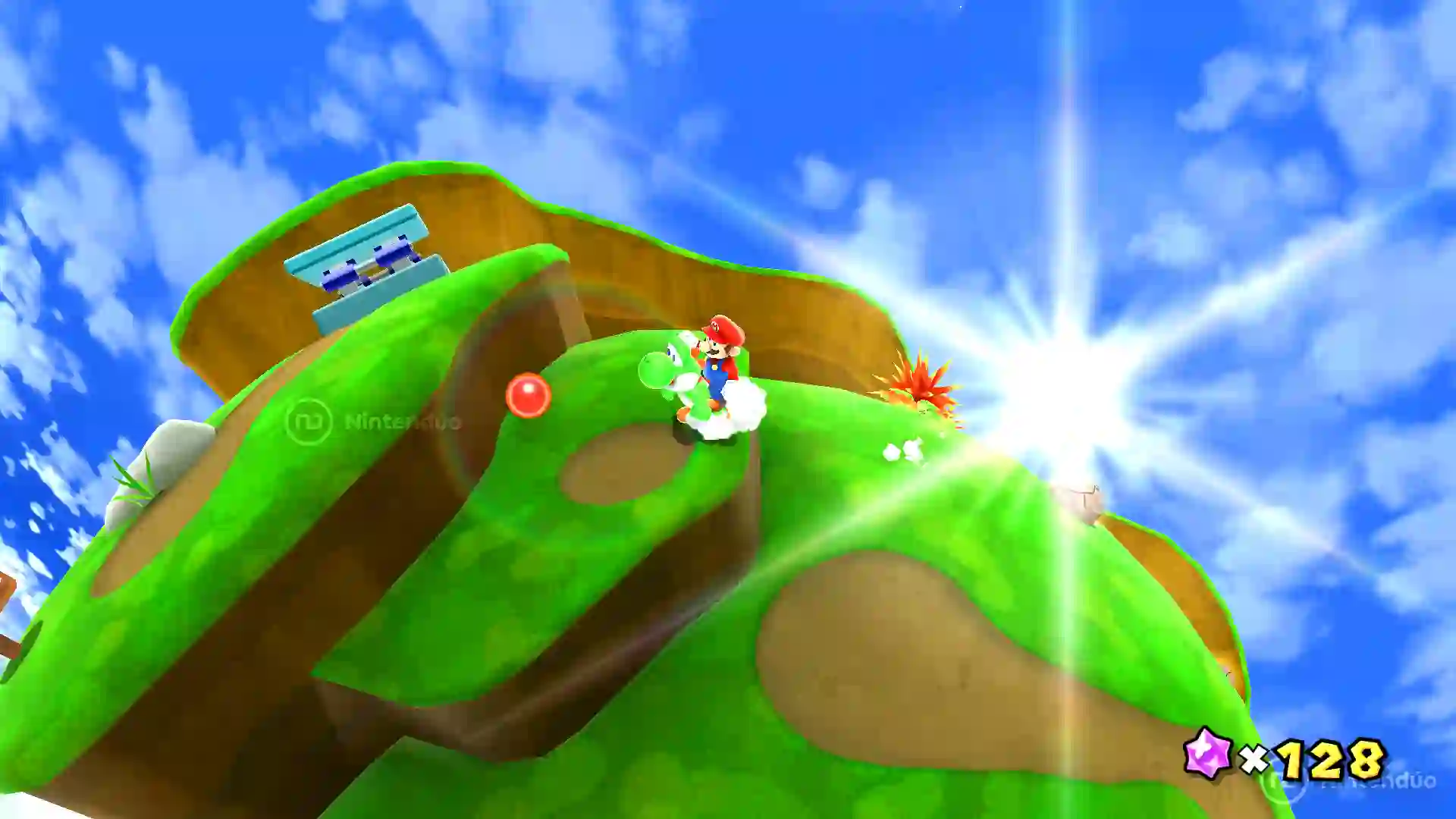 Mario montado en Yoshi en Super Mario Galaxy recorriendo una pequeña colina verde bajo un sol radiante.