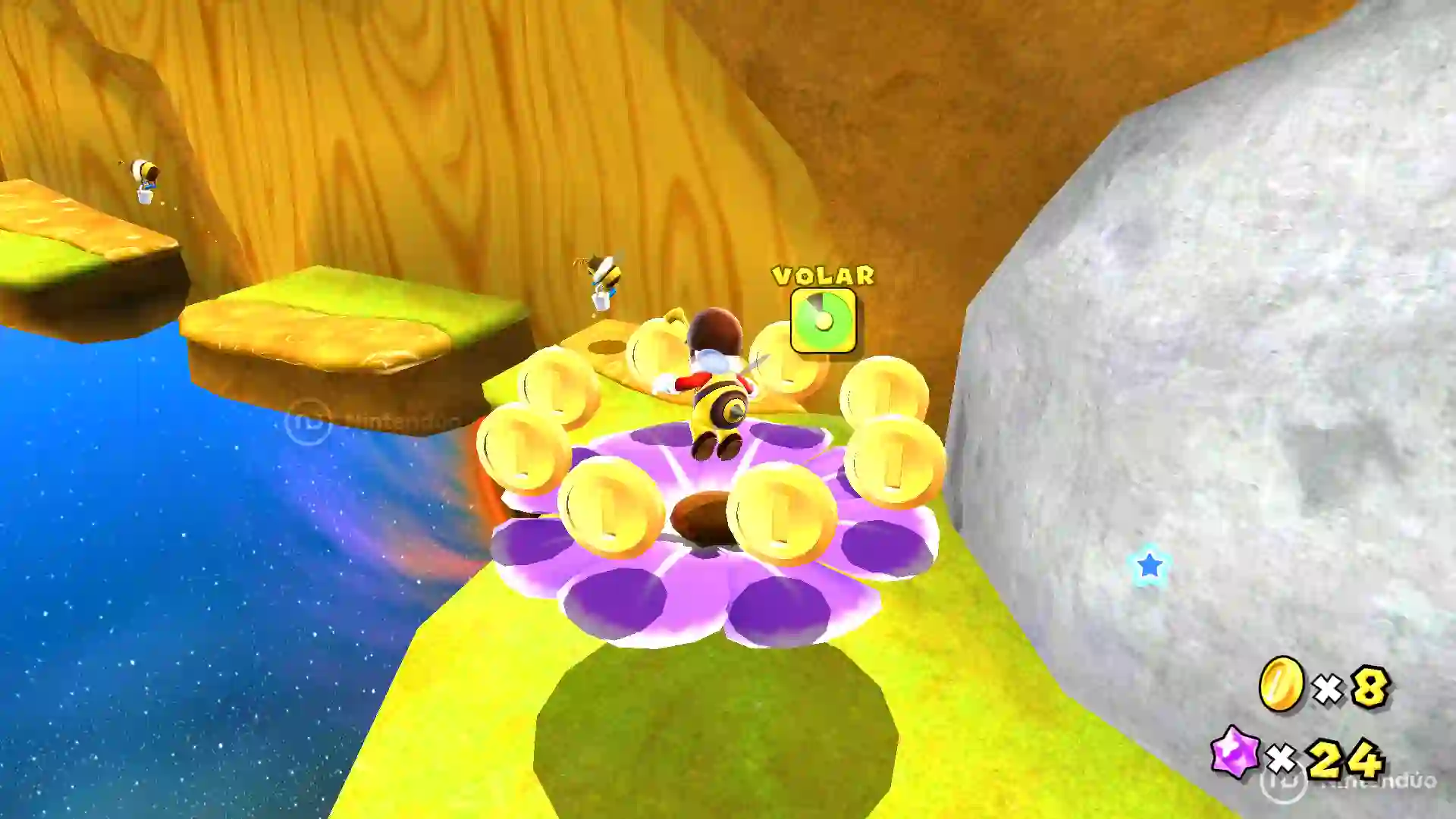 Mario abeja de Super Mario Galaxy volando dentro de un anillo de monedas doradas sobre una flor púrpura en un nivel aéreo.