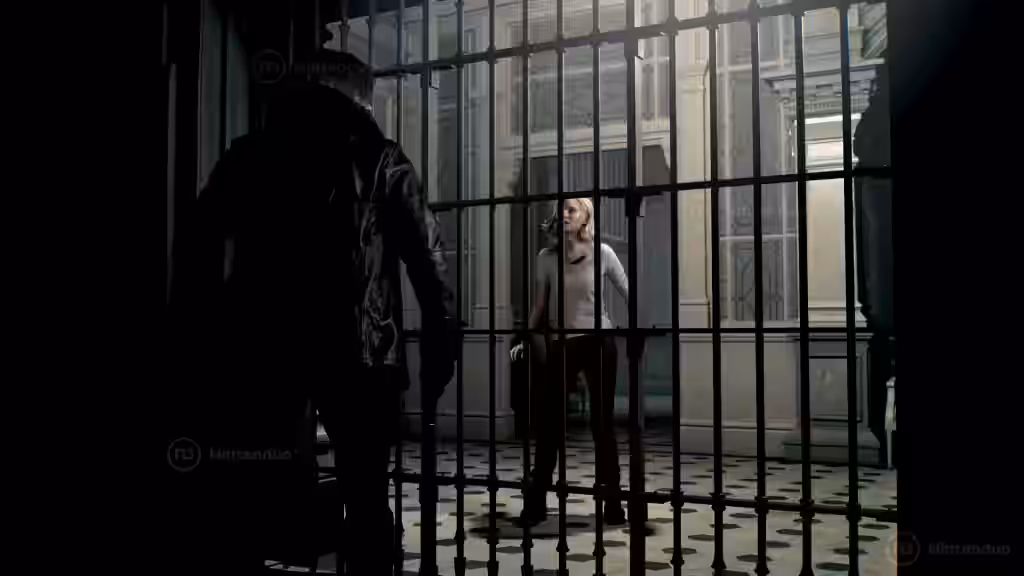 Dos personajes en una celda con barrotes de metal en Resident Evil Requiem - 01, uno con chaqueta oscura en el exterior y otro rubio dentro con ropa clara bajo iluminación tenue.